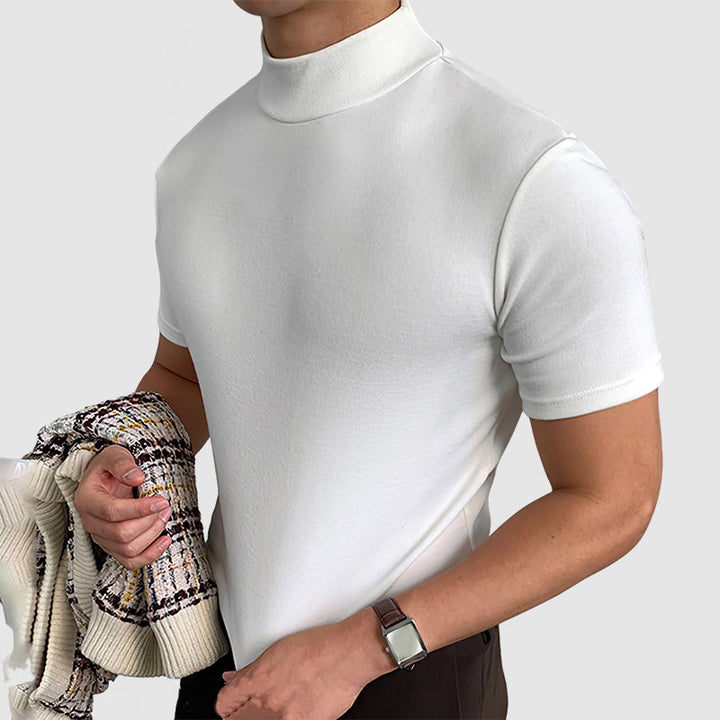 Model in the white mock-neck tee holding a patterned knit cardigan in one hand, wearing a wristwatch.