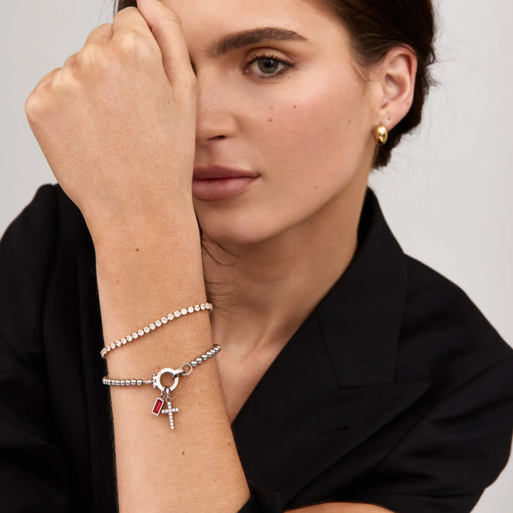 Model wearing a silver-tone bead bracelet with red stone and cross charms, layered with a crystal bracelet.