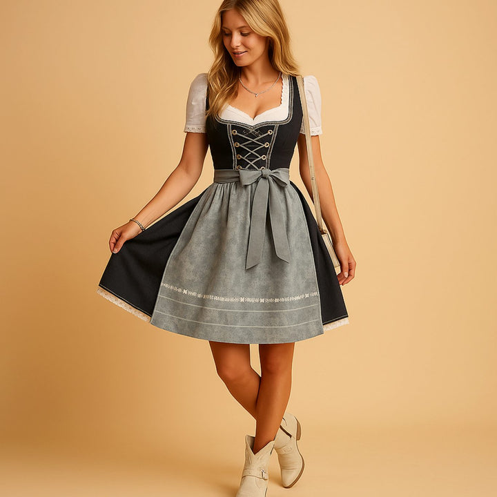 Dark dirndl with gray apron bow, holding out the skirt and wearing cream ankle boots
