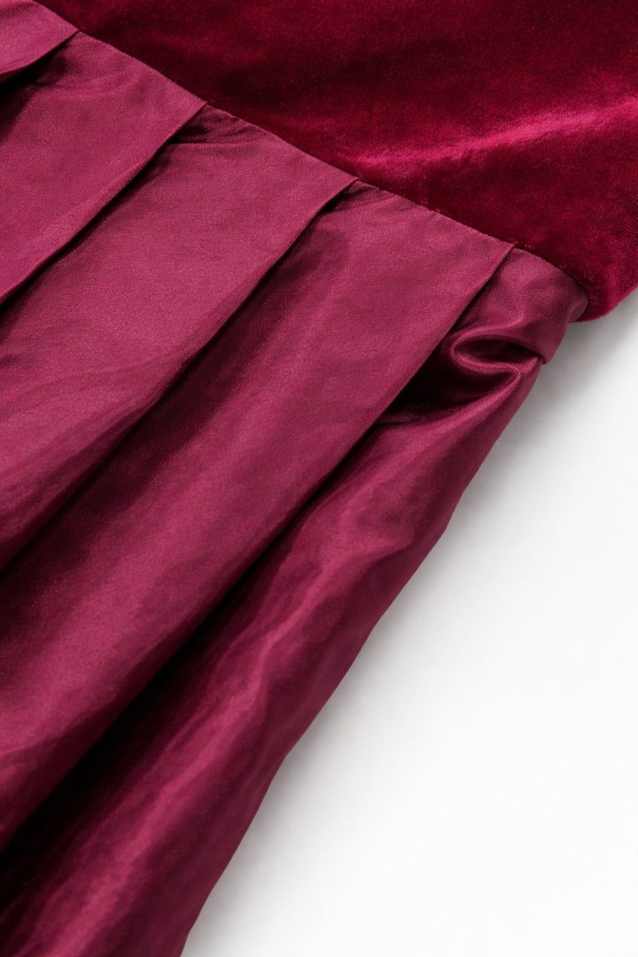 Close-up detail of the burgundy velvet bodice meeting the glossy pleated satin skirt at the waist seam.