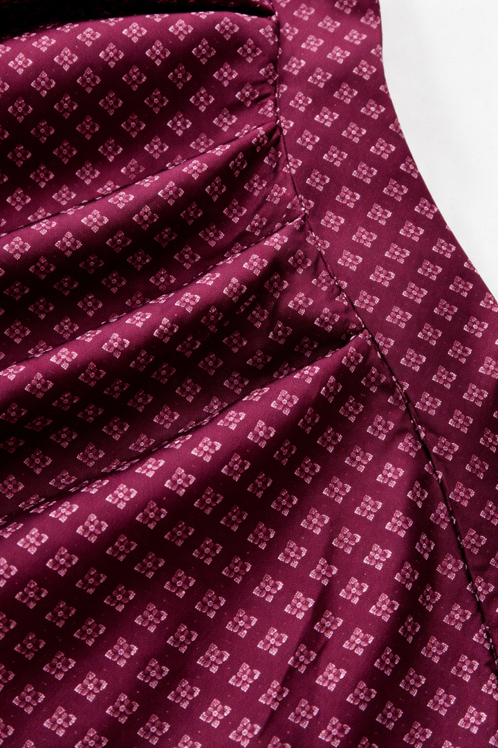 Detail of the apron fabric showing a small light floral diamond motif on burgundy, with gathered pleats and stitching.