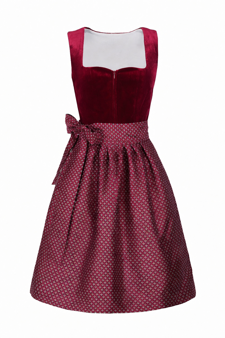 Front view of the burgundy velvet dirndl with a patterned jacquard apron tied in a side bow over the skirt.