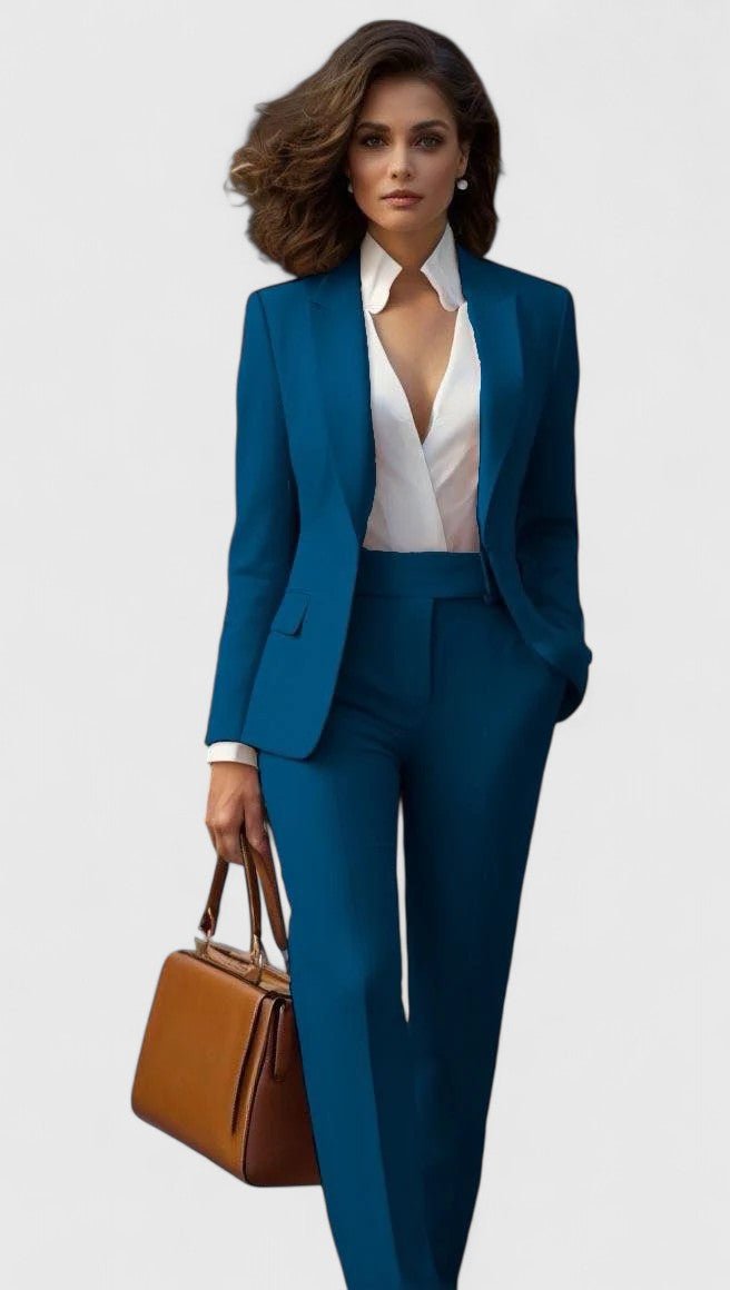 Model wearing the suit in teal blue with a white blouse, carrying a tan leather handbag 2