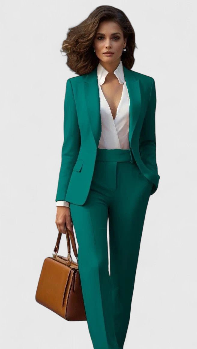 Model wearing the suit in emerald green over a white blouse, one hand in pocket, tan handbag 4