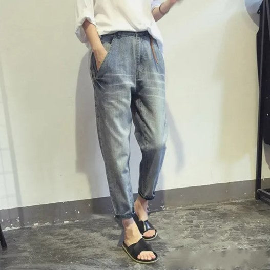 Person in blauer Jeans und weißem Hemd, lässiger Stil, schwarze Sandalen, Betonboden.