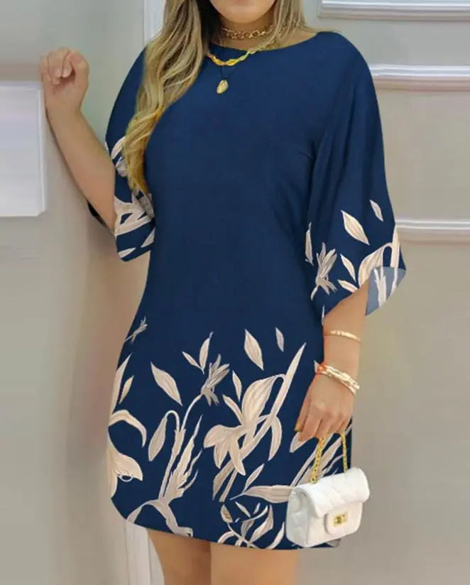 Frau in blauem Kleid mit Blumenmuster, goldene Accessoires, weiße Handtasche.