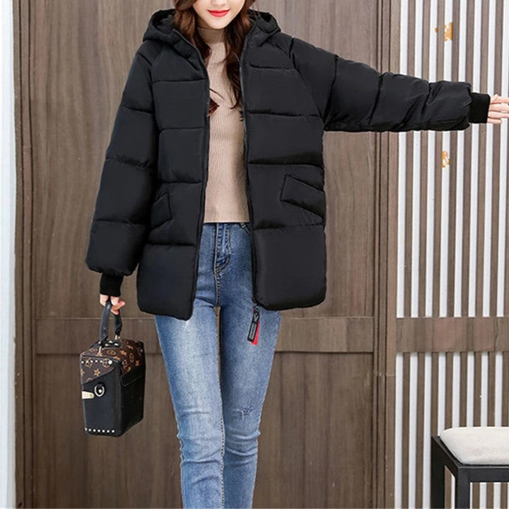 Frau in schwarzer Daunenjacke, blaue Jeans, hält schwarze Handtasche, Wintermode.