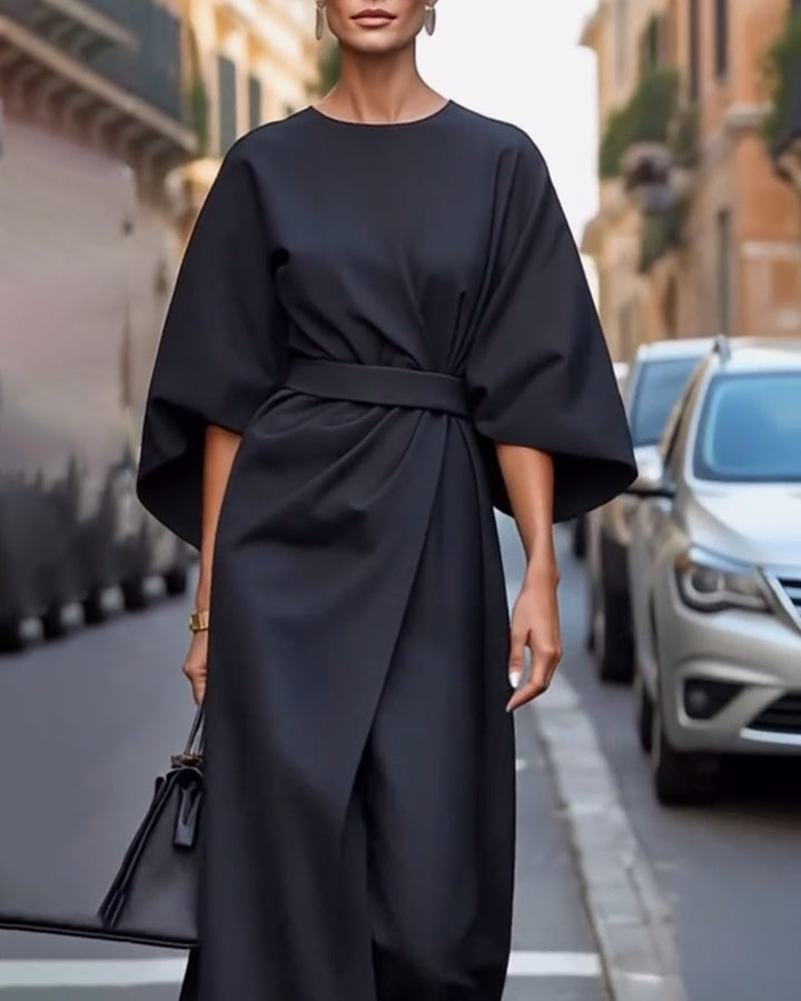 Woman in a black wrap-style dress with a tied belt and drop earrings, standing beside parked cars 4