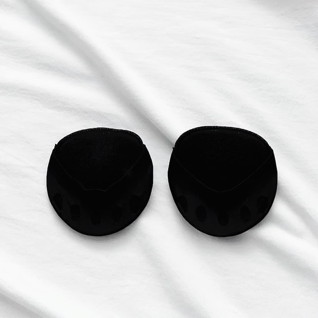 Pair of black forefoot cushions with toe openings laid flat on wrinkled white fabric.