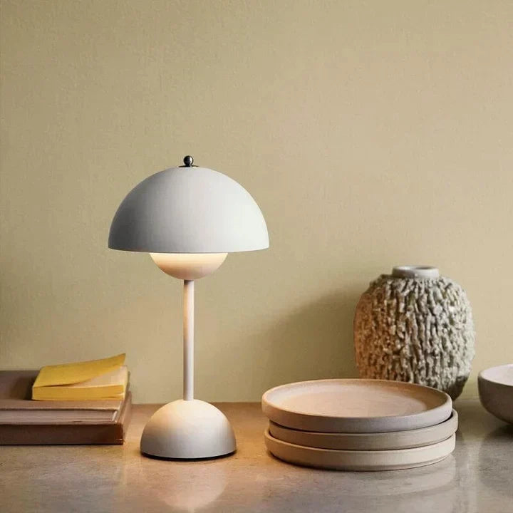 Grey metal rechargeable USB table lamp on a stone shelf beside plates, a vase and books.