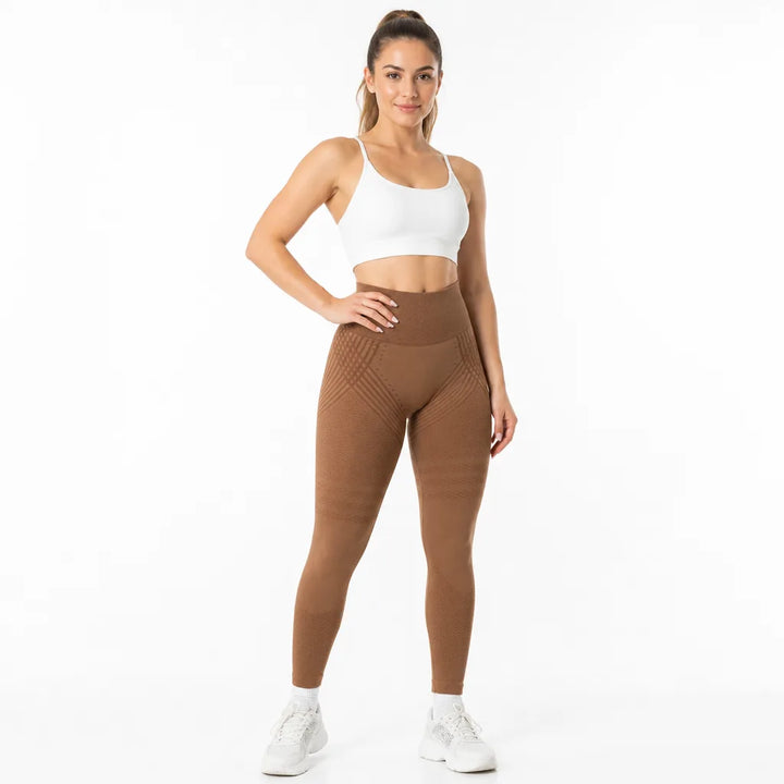 Model standing in caramel brown high-waisted leggings with textured hip and thigh stripes, a white strappy sports bra, and white sneakers. 17