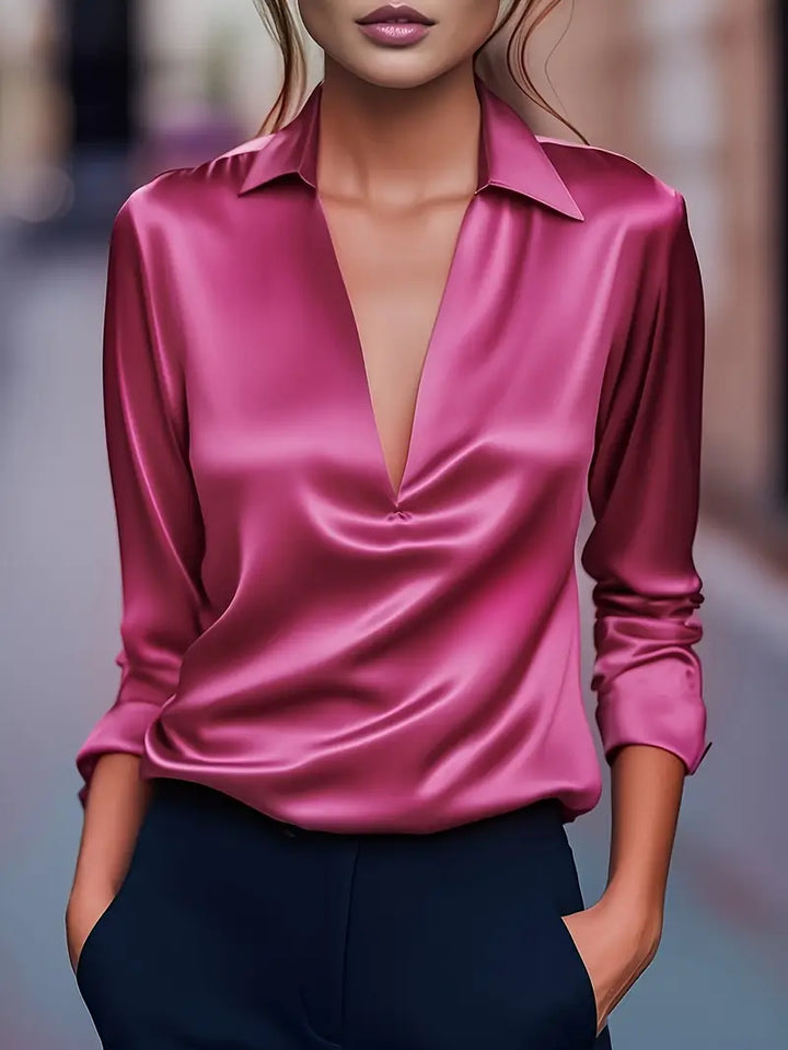 Model wearing the long-sleeve satin blouse in bright fuchsia pink with a deep V-neck and small gathered point.