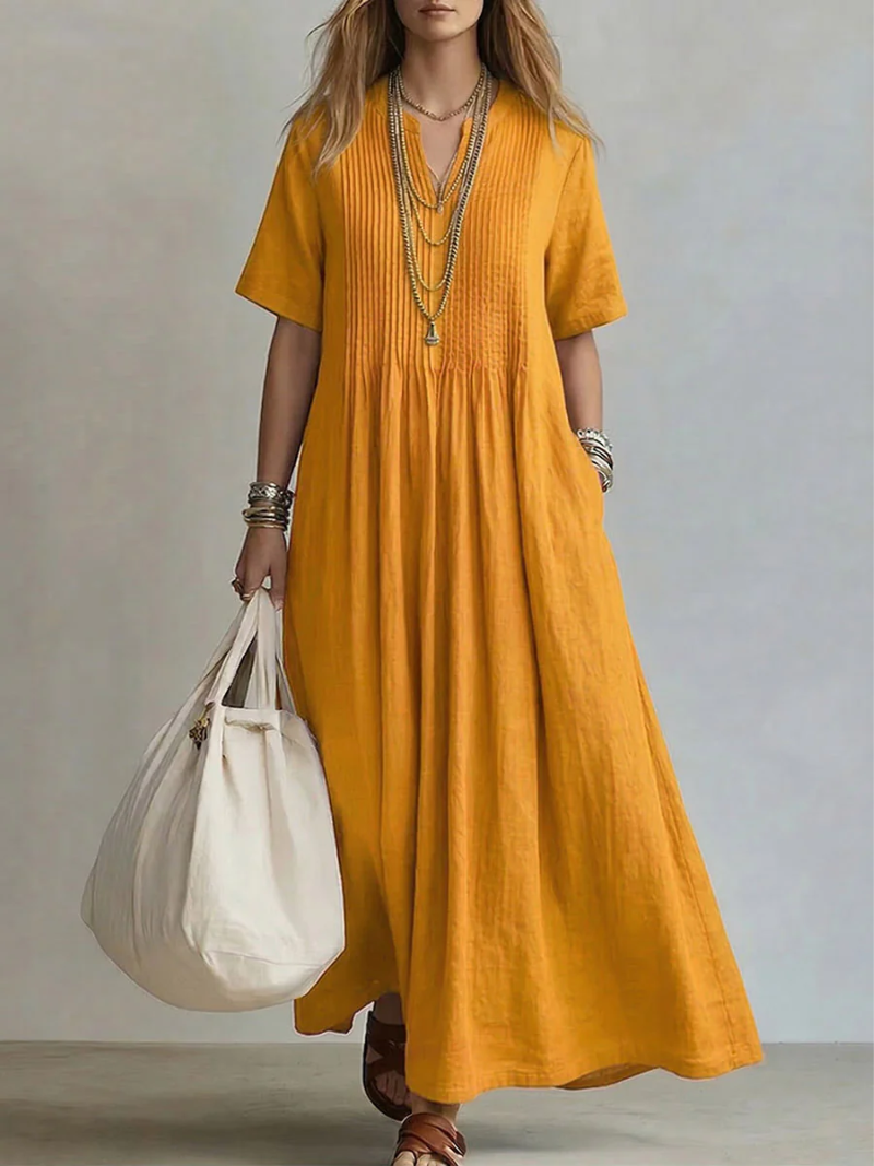 Model wears the short-sleeve pleated dress in golden mustard yellow, detail.