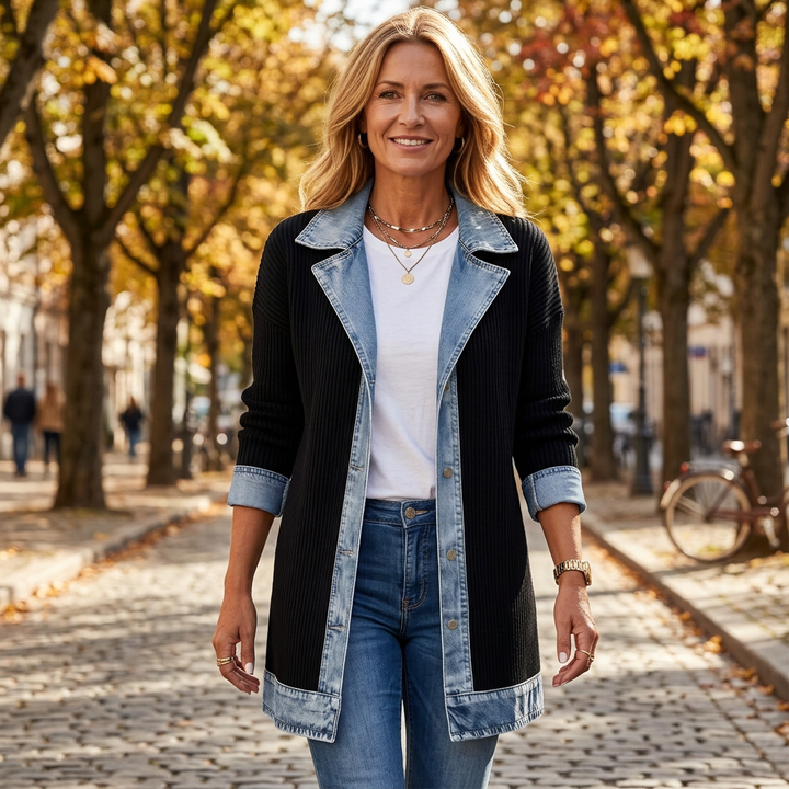 Smiling woman in a black ribbed coat with light denim lapels and cuffs, walking down a cobblestone street in autumn. 1