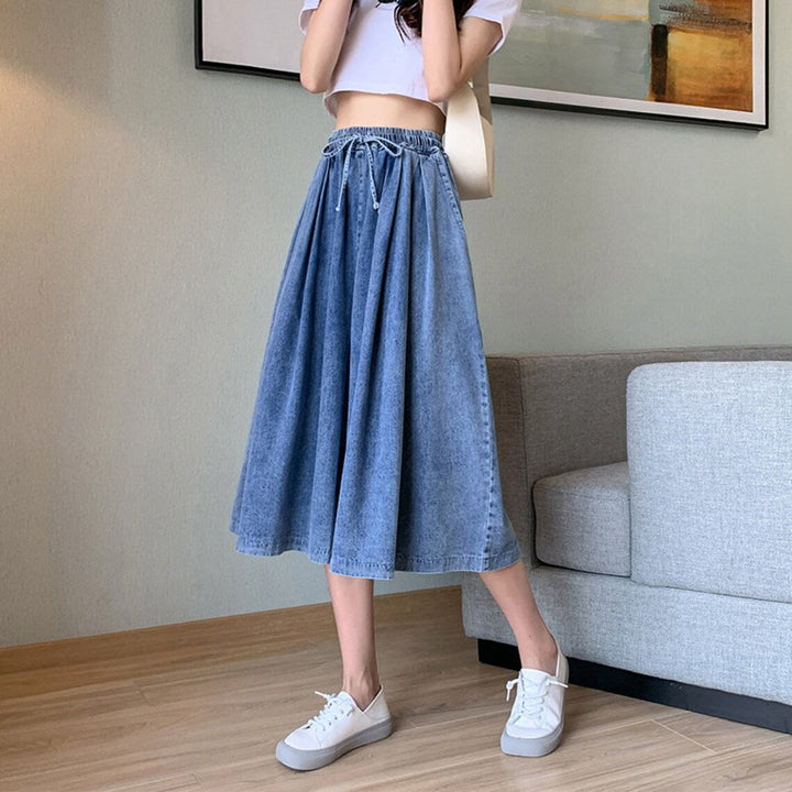 Frau in blauem Jeansrock und weißem T-Shirt, steht in modernem Wohnzimmer, trägt weiße Sneaker.
