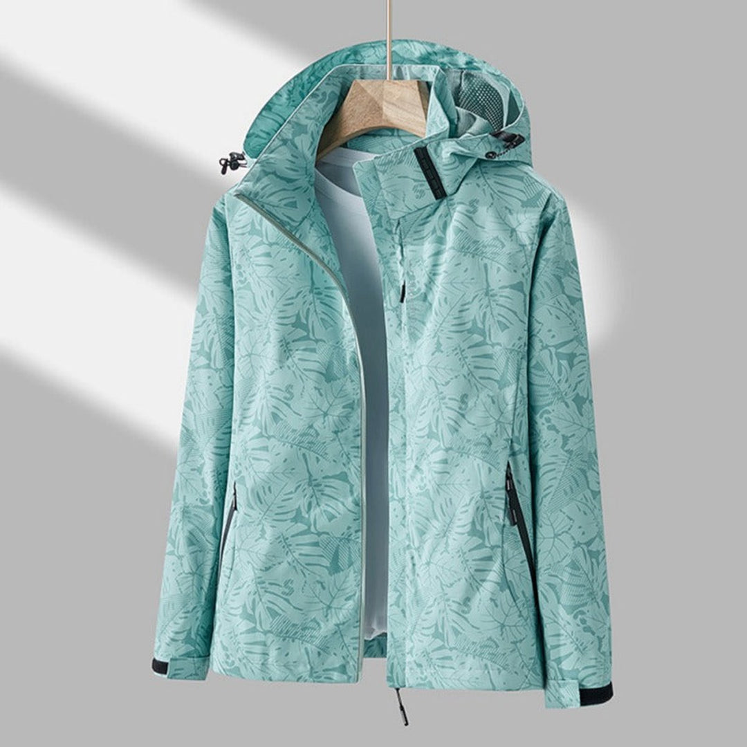 Mint green hooded jacket with a tonal leaf print, hanging open over a pale top, showing black zip pockets and cuff tabs. 7