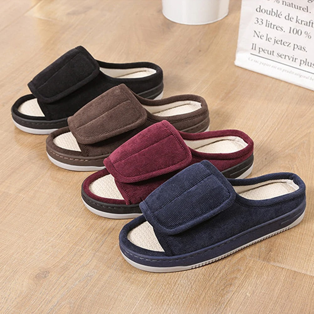 Four slippers in black, brown, burgundy and navy corduroy lined up on a wooden floor, each with a wide fold-over strap. 2