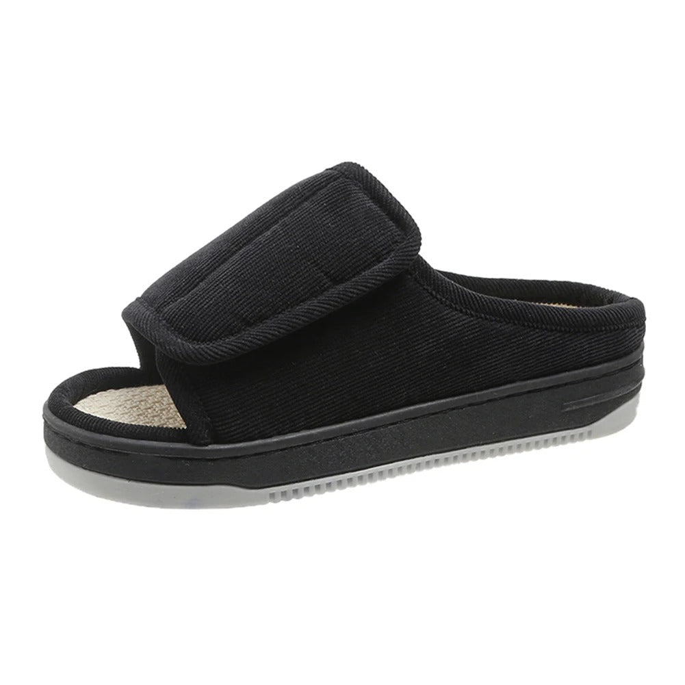 Black open-toe slipper with a wide fold-over strap, beige woven footbed and gray ridged sole, side view.