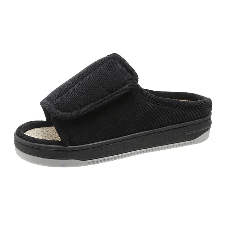 Black corduroy slipper detail on a white background with a wide fold-over strap, open toe and ribbed sole.