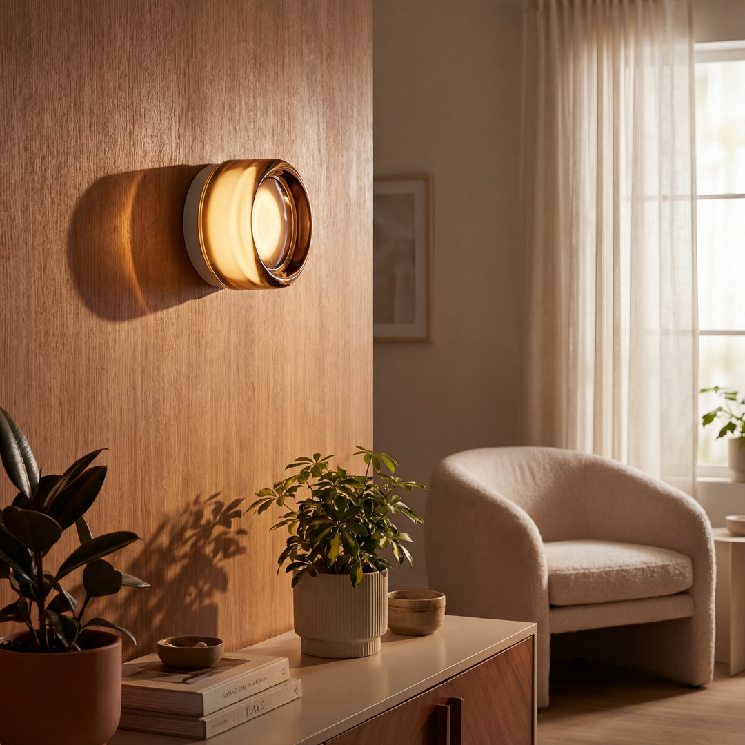 Amber glass sconce lit on a wood-paneled wall above a sideboard with plants, books, and a boucle armchair nearby. 2