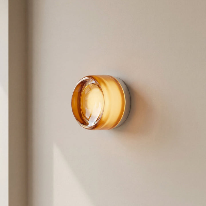 Close side view of the lit amber glass sconce on a beige wall, showing its thick rounded glass and white mount. 3