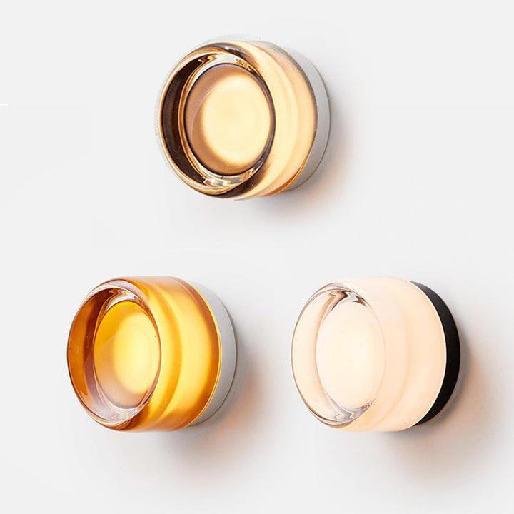 Three sconces arranged on a white wall: a lit smoky amber one on top, then amber and milky white versions below. 5