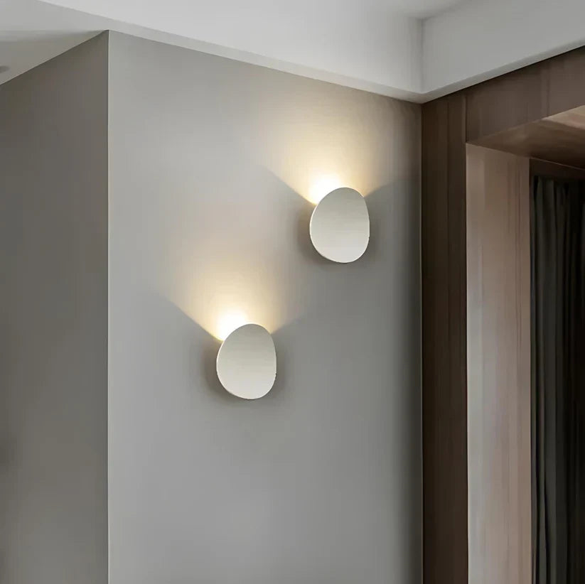 Two white oval wall lamps mounted at staggered heights on a gray wall, each casting a warm glow upward. 4