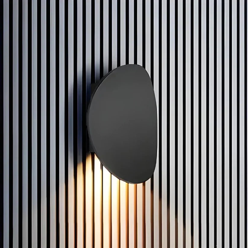 Black oval wall lamp on a vertical black-and-white slatted wall, light spilling downward across the stripes. 6