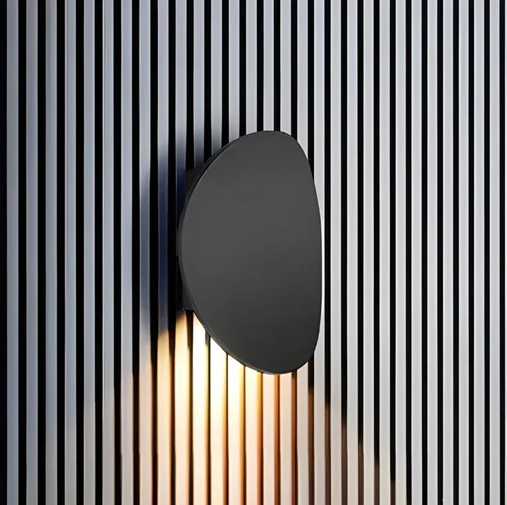 Black oval wall lamp on a vertical black-and-white slatted wall, light spilling downward across the stripes. 6