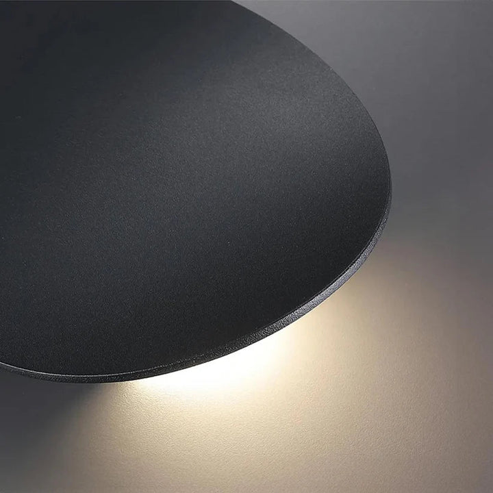 Close-up of the black disk's textured matte surface and thin edge, with warm light glowing beneath it. 9