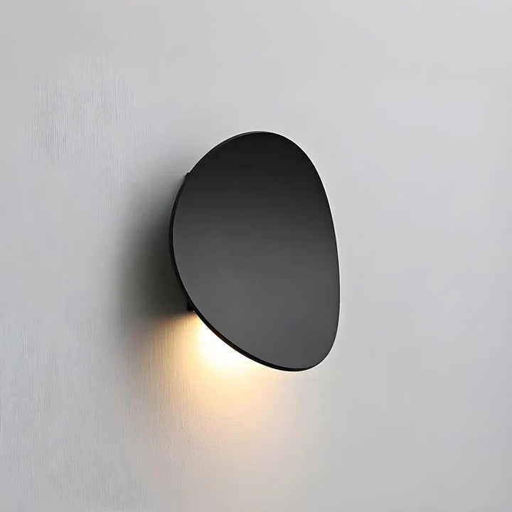 Black oval wall lamp seen from the side, tilted away from the wall with warm light shining downward. 11