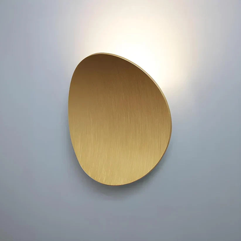 Oval wall lamp in a brushed gold finish with visible fine streaks, glowing softly behind its upper edge. 12