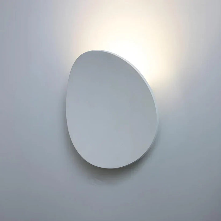 Oval wall lamp in a white finish mounted on a light wall, with warm light glowing behind its top edge. 13