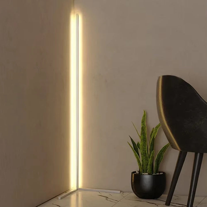 White corner floor lamp giving off warm light in a room corner beside a potted green plant and a dark chair. 4