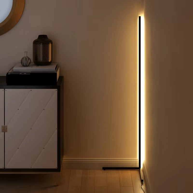 Black corner lamp casting warm light along a wall corner next to a white cabinet topped with books and vases. 2