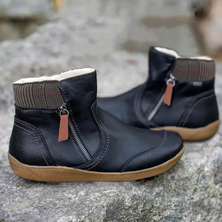 Pair of black ankle boots with side zipper, brown pull tab, plaid collar and light fleece lining, shown on a gray rock.