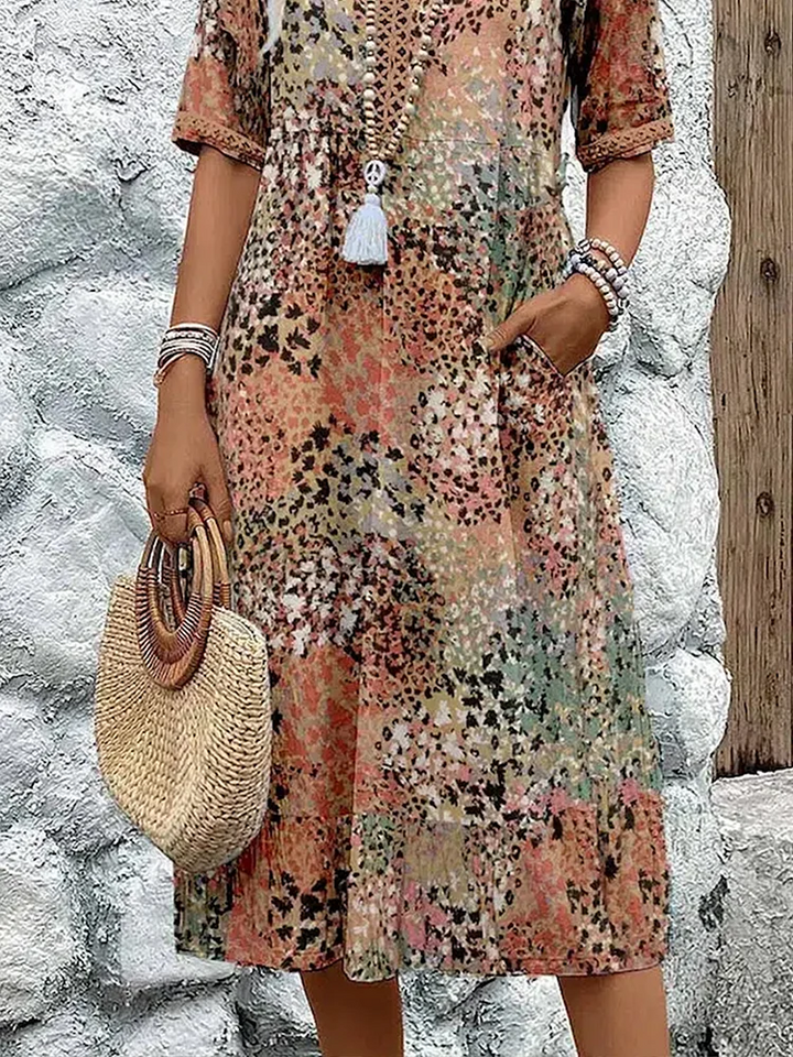 Lower view of the earthy speckled midi dress on a model, showing the flowing skirt, pocket, beaded bracelets and round straw handbag. 7