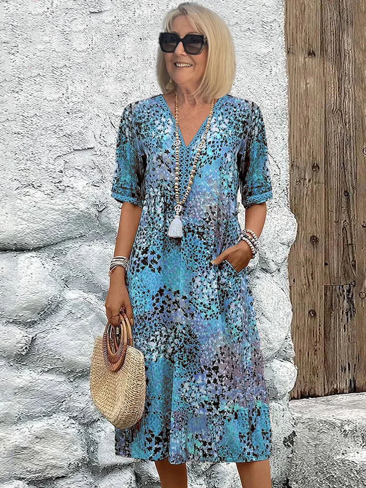 Same model and pose in the half-sleeve V-neck midi dress in a blue speckled print, with beaded necklace and straw bag. 2