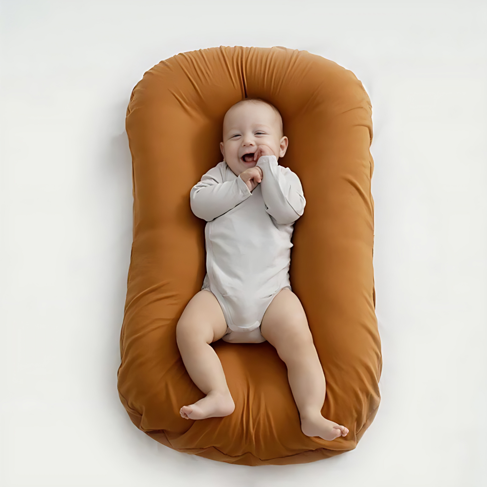 Overhead view of a smiling baby in a gray bodysuit lying on a rust-orange cushion 3