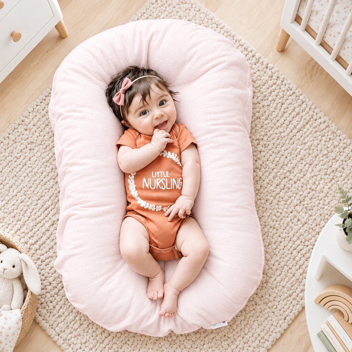 Smiling baby in an orange bodysuit and bow headband lies on a pink support pillow in a nursery 1