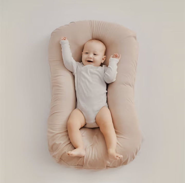 Happy baby with raised arms lies on a soft beige lounger, seen from above 7