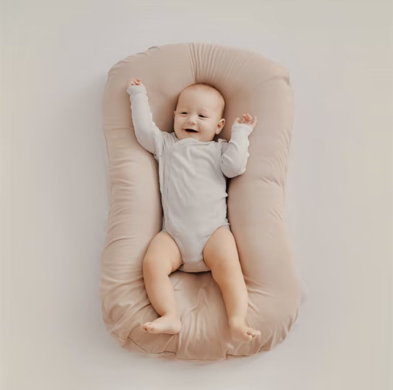 Happy baby with arms raised lies on a soft beige support pillow in an overhead view 7