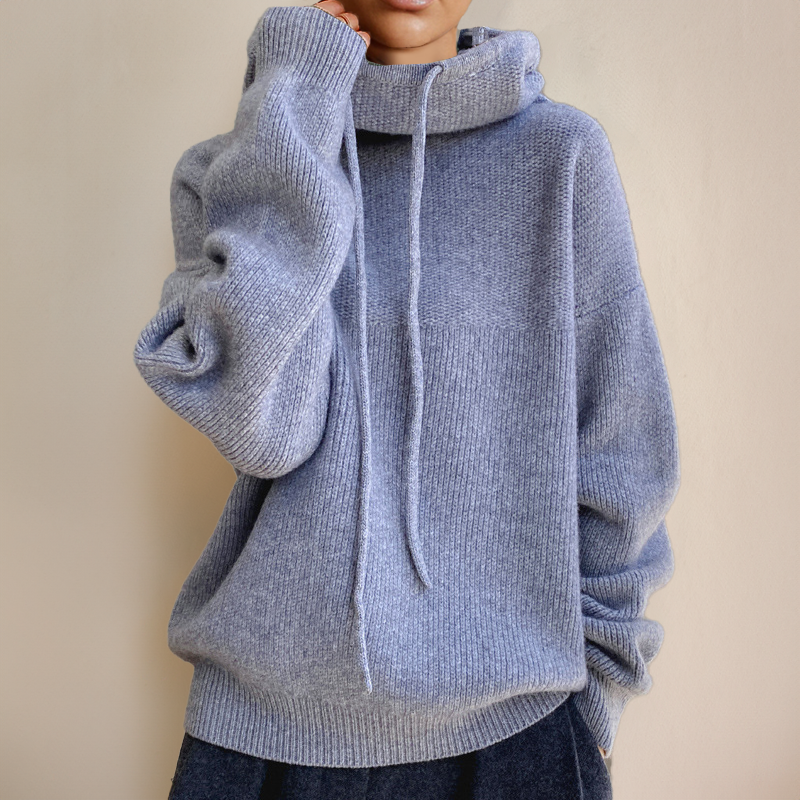 Blue-gray knit sweater with an oversized hood and long drawstrings, one hand raised to the neckline 6
