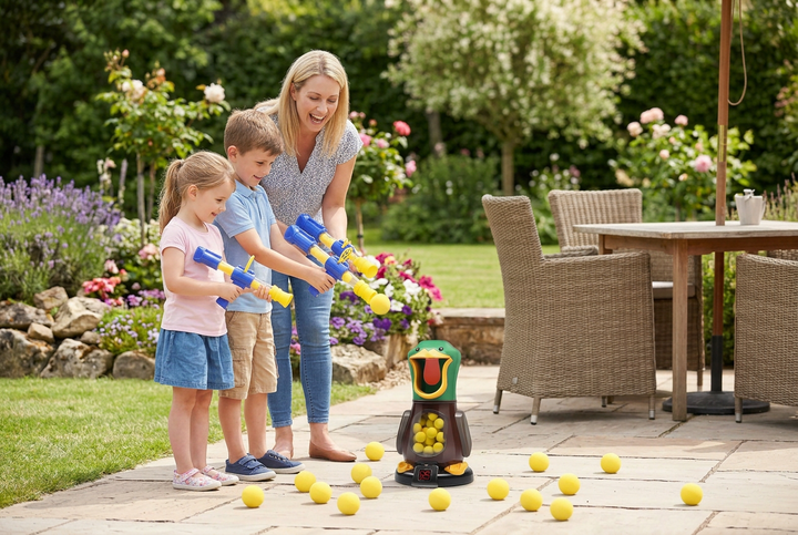 Smiling mother and two children aim blue-and-yellow foam ball blasters at a duck target on a sunny garden patio 1