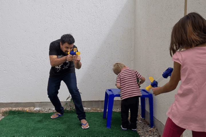 A man and two children play outdoors with blue-and-yellow launchers on a small patch of artificial grass 9