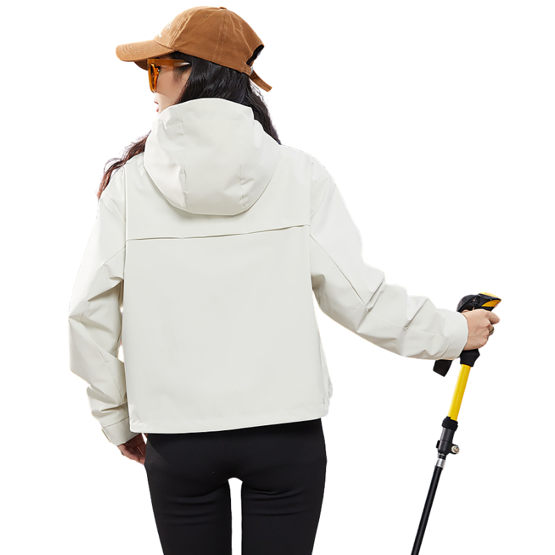Back view of the cream jacket showing the shaped hood and yoke seam, model holding a yellow trekking pole. 5