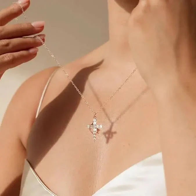 Woman in a white camisole holds up a rose gold cross pendant on a fine chain 1
