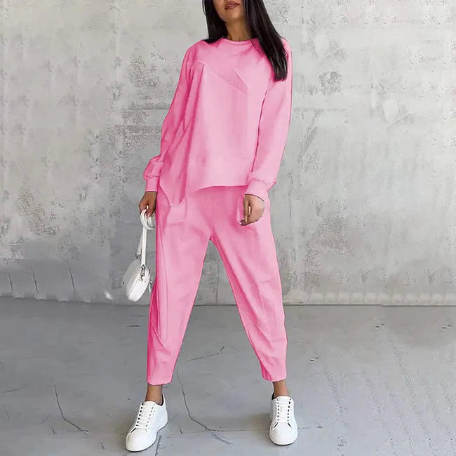 Woman wearing the bright pink version of the long-sleeve sweatshirt and tapered joggers, with white sneakers and a white bag.