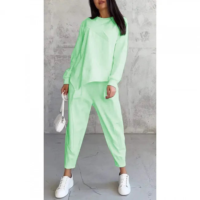 Woman wearing the mint green sweatshirt and jogger pants on a plain white background, with white sneakers and a small white bag.