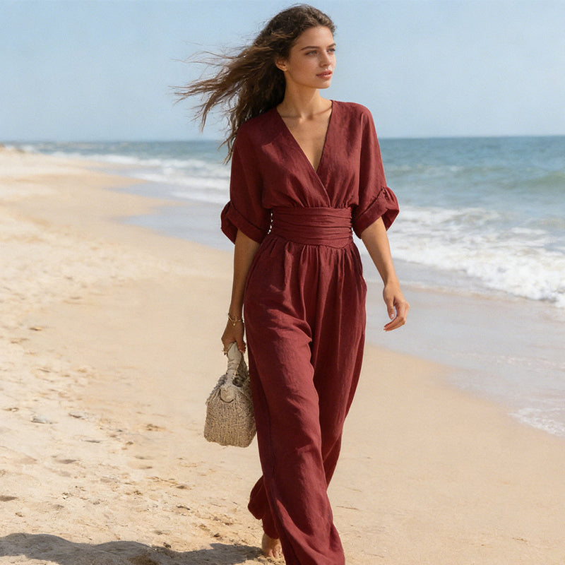 Another view of the burgundy women's elegant linen jumpsuit on a beach with wide-leg pants